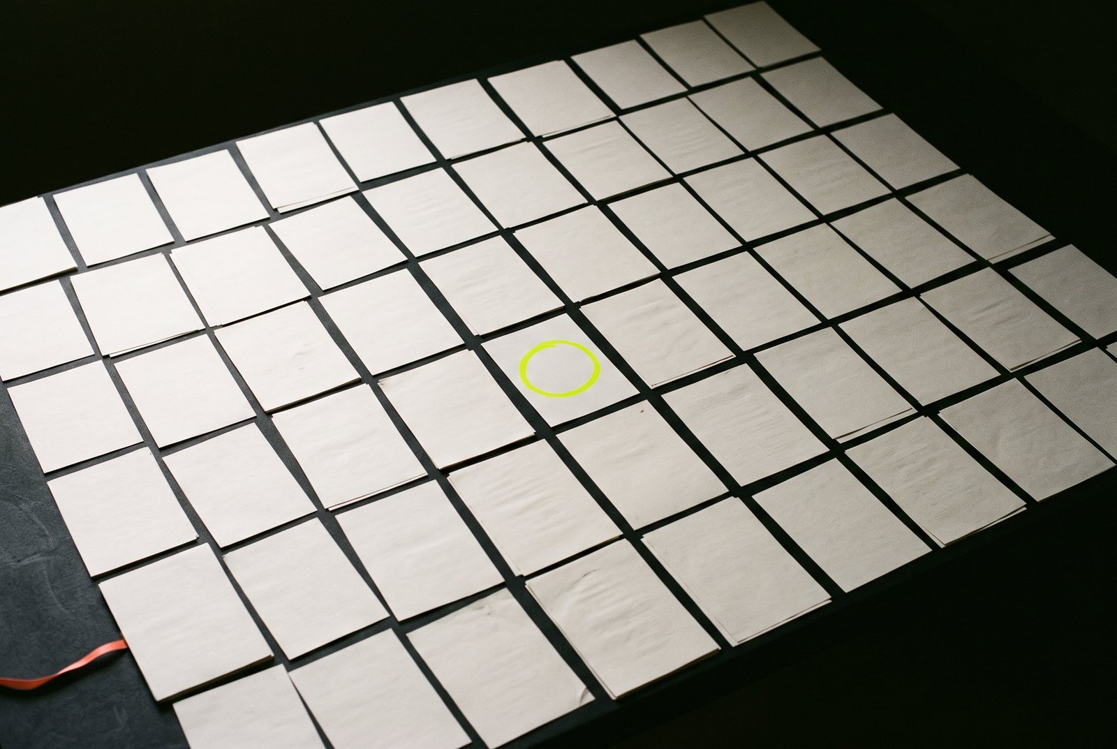 A grid of identical plain pages on a dark surface, with a single lime circle drawn on one page near the centre